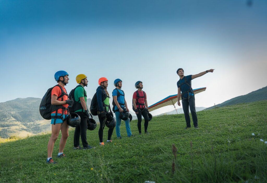 A group of people preparing for a beginner speed flying course on a grassy mountain slope with an instructor guiding them.