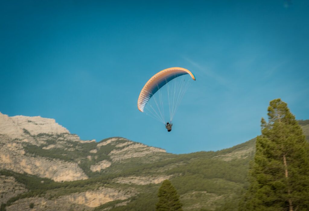 A paraglider flying over mountains in clear blue sky, showing smooth and fast gliding motion.