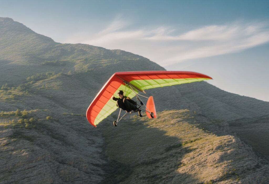 A speed flyer gliding over mountainous terrain with a brightly colored wing, demonstrating smooth and controlled flight.