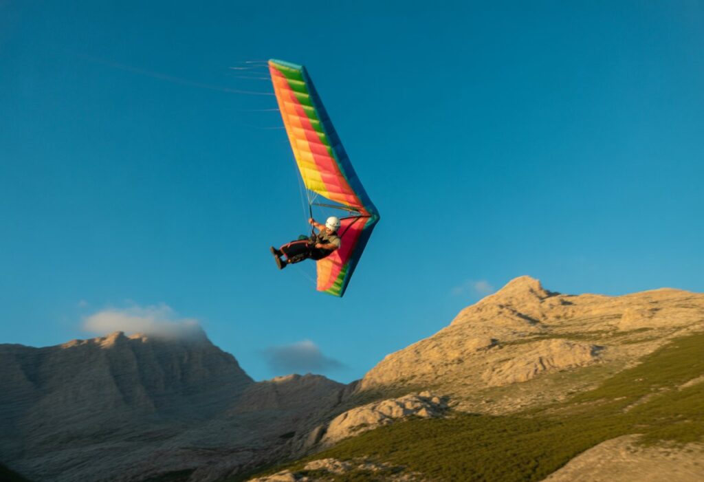 A person speed flying with a colorful wing near mountains under a clear sky.