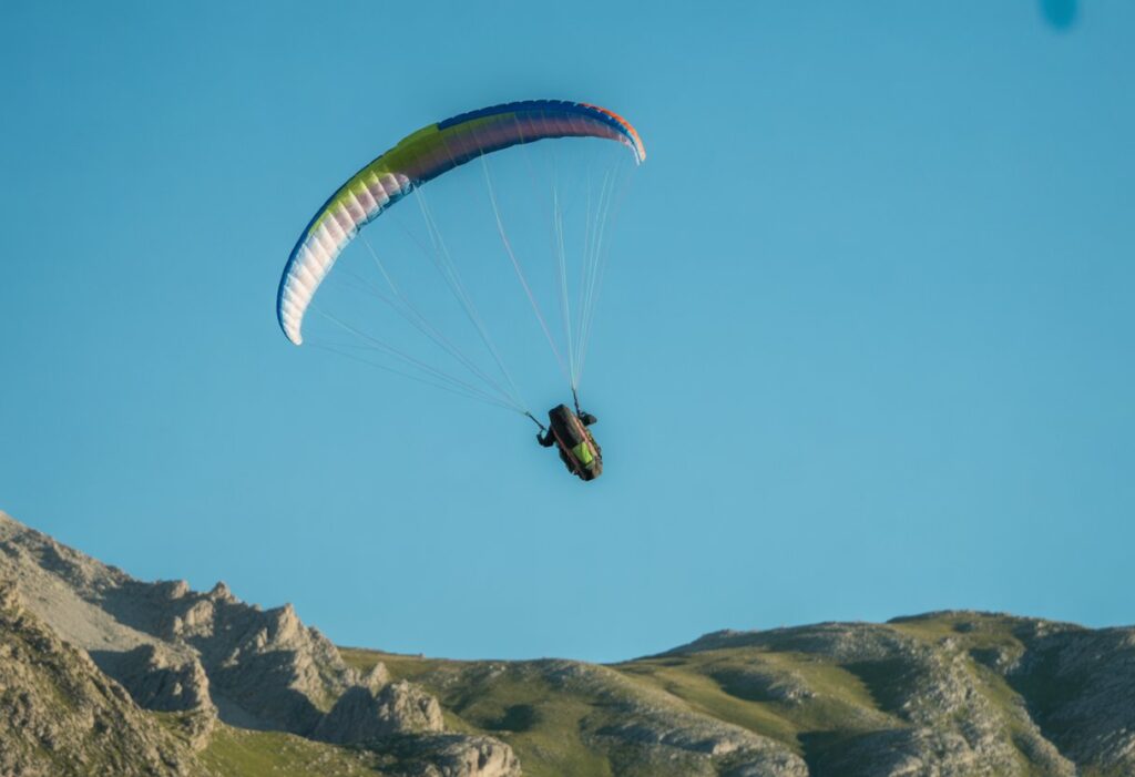 A paraglider performing a flip in mid-air above misty mountains with a colorful parachute.
