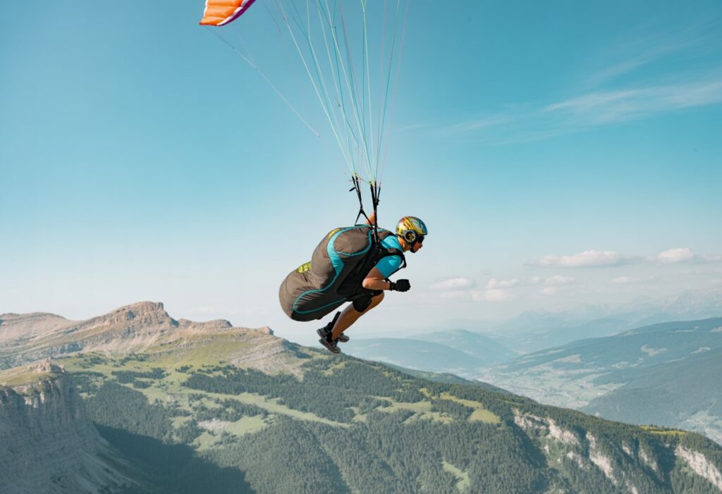 A paraglider pilot performing acrobatic maneuvers in the sky above a mountainous landscape.
