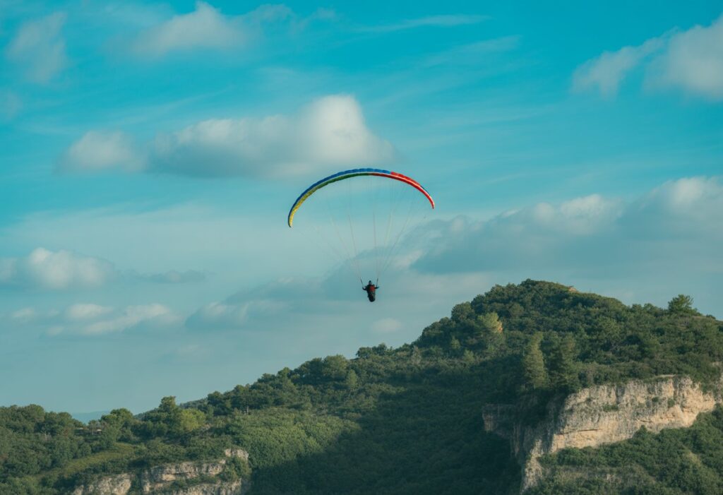 A paraglider circling in the sky above green mountains under a clear blue sky.