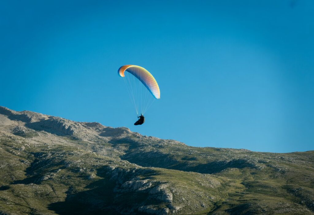 A paraglider performing an aerobatic loop over mountainous terrain under a clear blue sky.