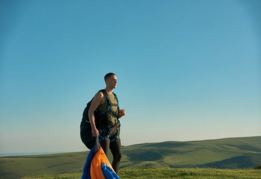 A fit person standing on a hilltop preparing for thermal flying with a glider under a clear blue sky and rolling hills in the background.