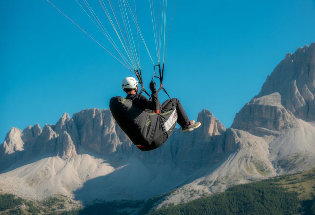 A paraglider flying over mountains with safety gear on a clear sunny day.